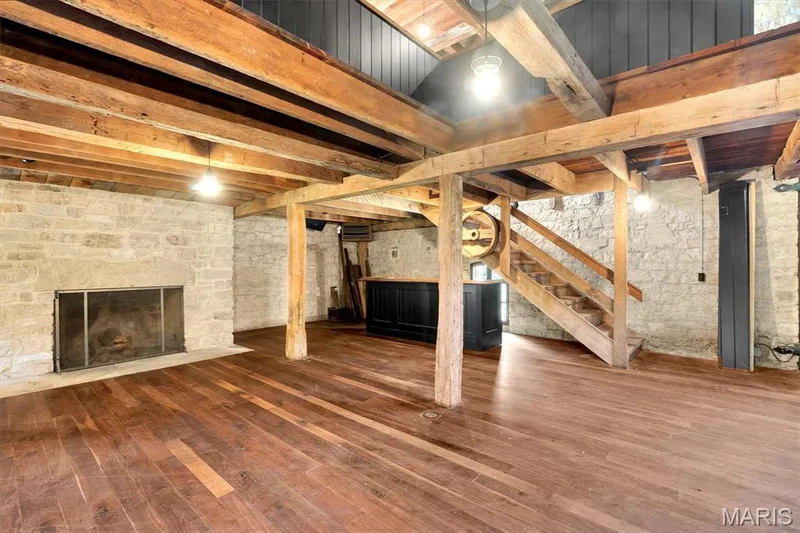 Hardwood flooring, exposed wood beams, stone accent wall, built-in fireplace, and a wood staircase — 2275 Highway F, Defiance, MO 63341