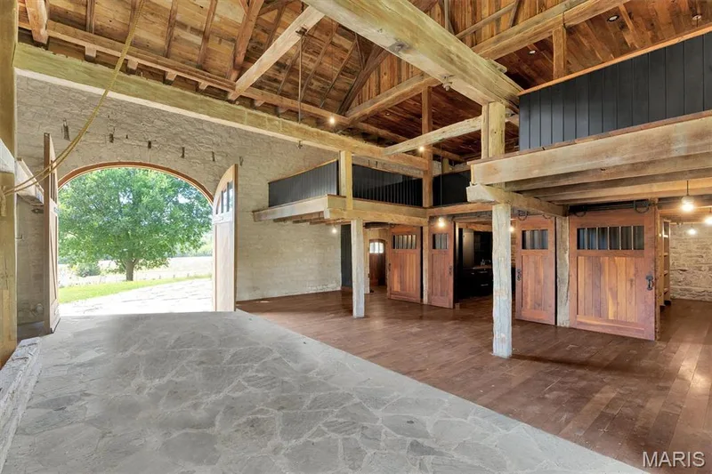 Exposed wood beam ceiling, wood-finish flooring, stone wall accents, arched entryway, and multiple wooden sliding doors — 2275 Highway F, Defiance, MO 63341