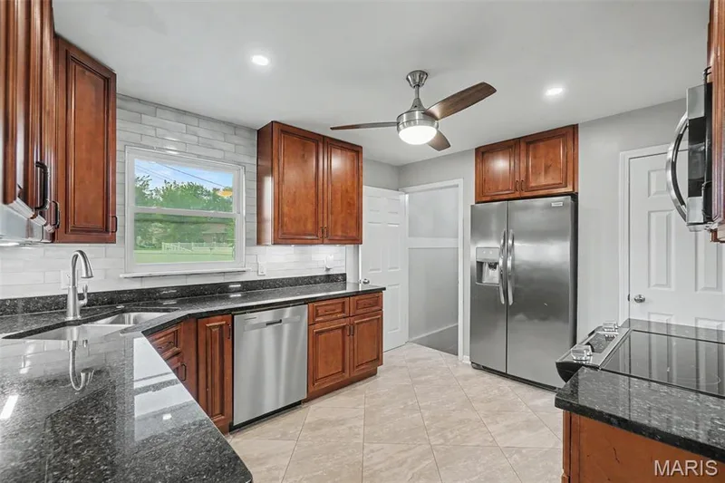 Kitchen featuring wood cabinetry, solid surface countertops, subway tile backsplash, and stainless steel appliances. — 502 Pine Street, St Charles, MO 63301