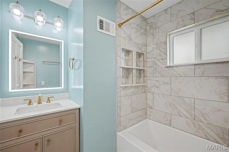 Updated bathroom with integrated vanity sink and gold-tone fixtures, illuminated mirror, three-light vanity bar. The marbled tile shower surround with recessed niches, and deep bathtub provide that spa feeling for everyday living. — 502 Pine Street, St Charles, MO 63301