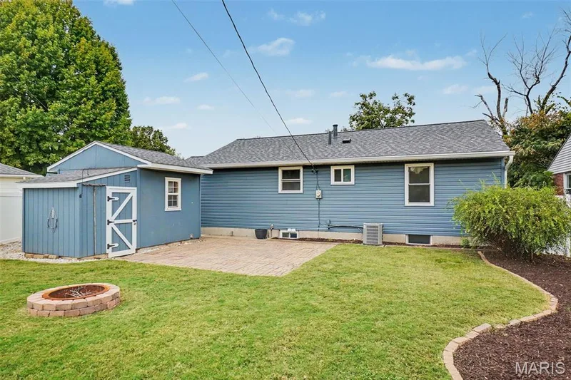 Expansive rear yard featuring a paved patio area, a detached storage shed, a built-in fire pit, and defined landscaping beds with mulch. — 502 Pine Street, St Charles, MO 63301