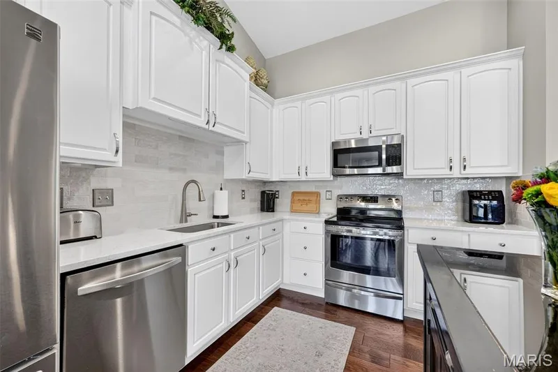 Kitchen featuring white shaker-style cabinetry, stainless steel appliances, a tile backsplash, light-toned countertops, and wood-finish flooring — 14737 Ladue Bluffs Crossing Drive, Chesterfield, MO 63017