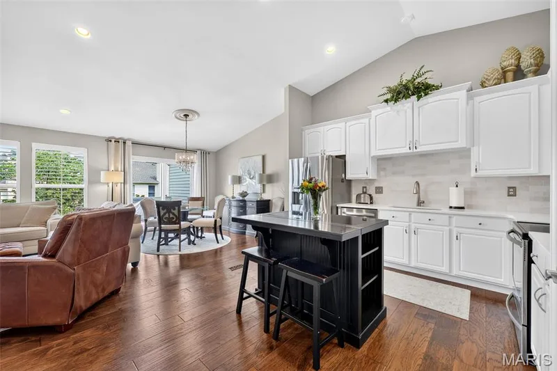 Vaulted ceiling, wood flooring, white cabinetry, stainless steel appliances, and a black kitchen island with countertop seating — 14737 Ladue Bluffs Crossing Drive, Chesterfield, MO 63017
