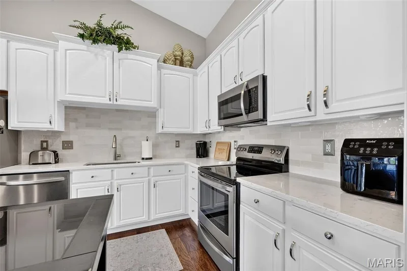 White cabinetry with stainless steel appliances, light-toned countertops, and a tiled backsplash — 14737 Ladue Bluffs Crossing Drive, Chesterfield, MO 63017