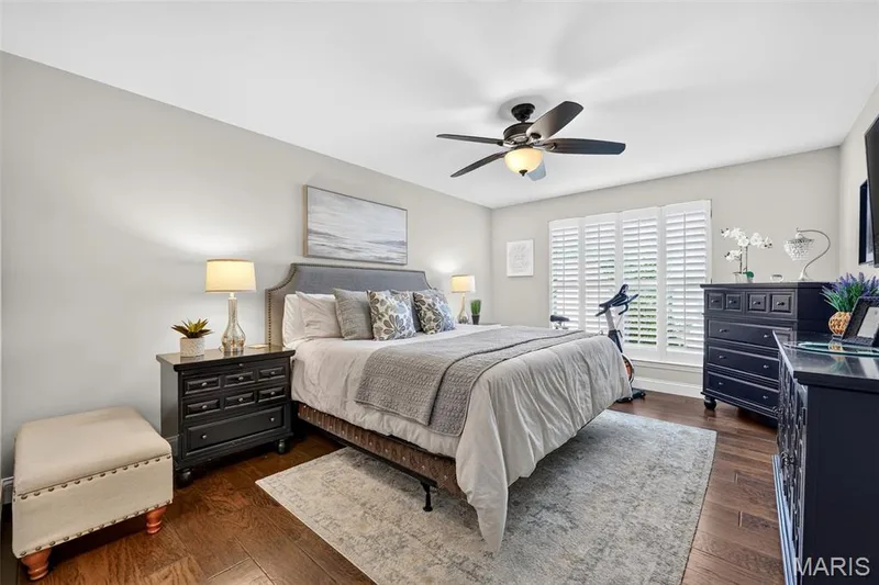 Primary bedroom with wood flooring, ceiling fan with integrated lighting, window with plantation shutters, and light gray wall paint — 14737 Ladue Bluffs Crossing Drive, Chesterfield, MO 63017