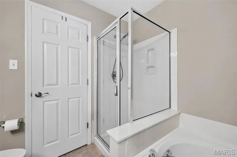 Glass-enclosed shower with a built-in shower caddy, adjacent to a white paneled door — 14737 Ladue Bluffs Crossing Drive, Chesterfield, MO 63017