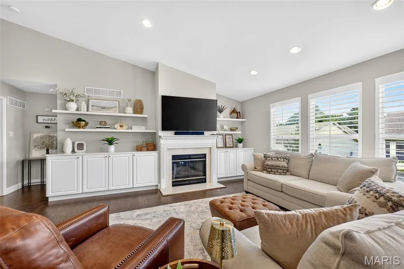Spacious living area featuring a fireplace, built-in cabinetry, floating shelves, recessed lighting, and multiple windows with white louvered shutters — 14737 Ladue Bluffs Crossing Drive, Chesterfield, MO 63017
