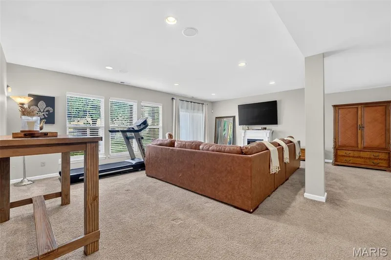 Basement recreation room with walkout door recessed lighting, light-toned carpeting, multiple windows with blinds, and a white fireplace mantel — 14737 Ladue Bluffs Crossing Drive, Chesterfield, MO 63017
