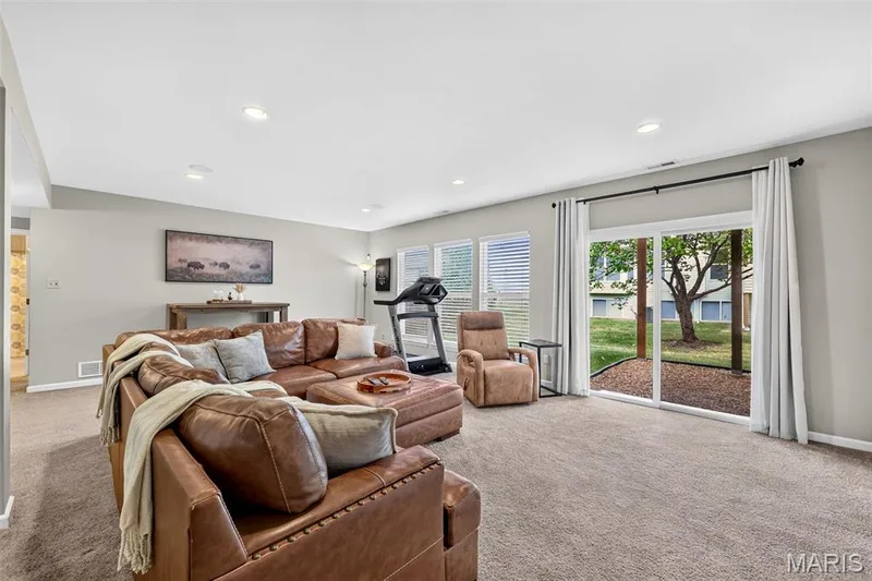 Recessed lighting illuminates the carpeted living space, featuring neutral wall tones and a sliding glass door — 14737 Ladue Bluffs Crossing Drive, Chesterfield, MO 63017