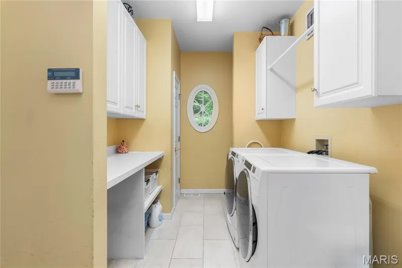 Laundry area featuring white tile flooring, white shaker-style cabinetry, and a built-in countertop with shelving — 19342 Dogwood Valley Court, Wildwood, MO 63038