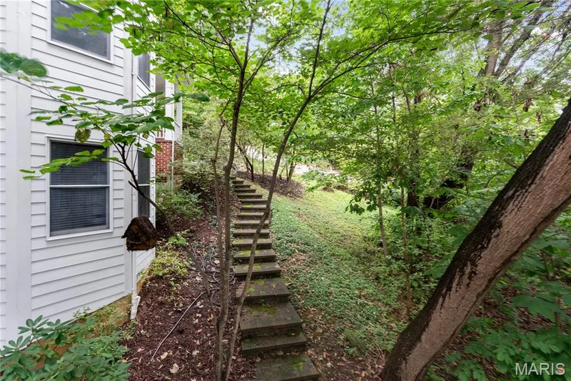 Wooded exterior with mature trees, a sloped landscaped yard, and a stone-stepped pathway — 19342 Dogwood Valley Court, Wildwood, MO 63038