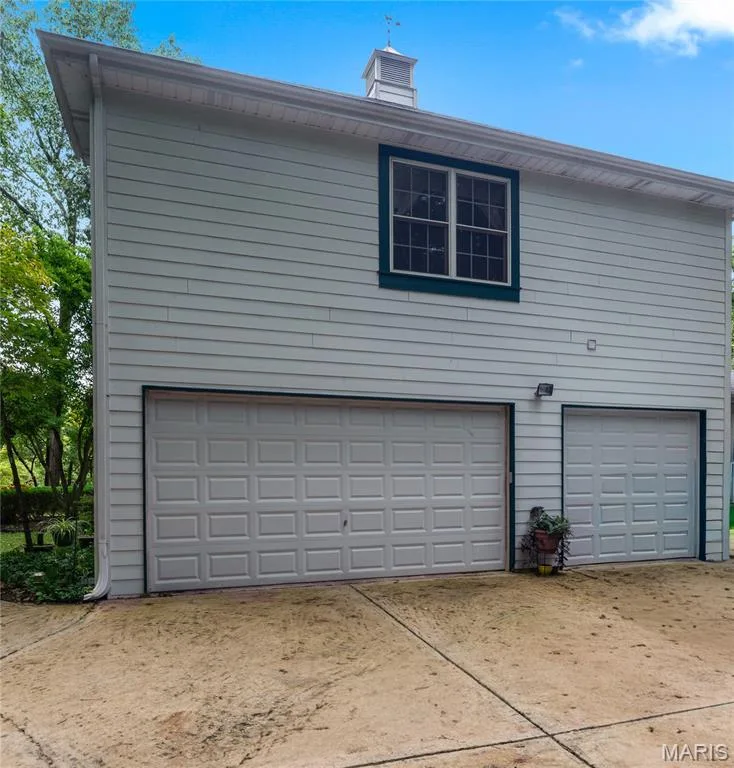 Three-car garage with panel-style doors, overhead lighting, and upper-level window with a cupola accent — 19342 Dogwood Valley Court, Wildwood, MO 63038