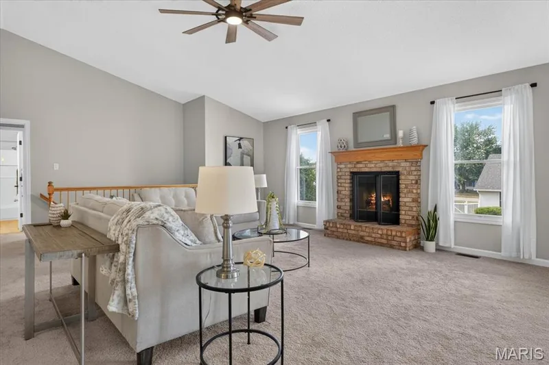 Vaulted ceiling with a ceiling fan, brick fireplace with a wood mantel, and carpeted flooring — 89 Gregory Court, Wentzville, MO 63385