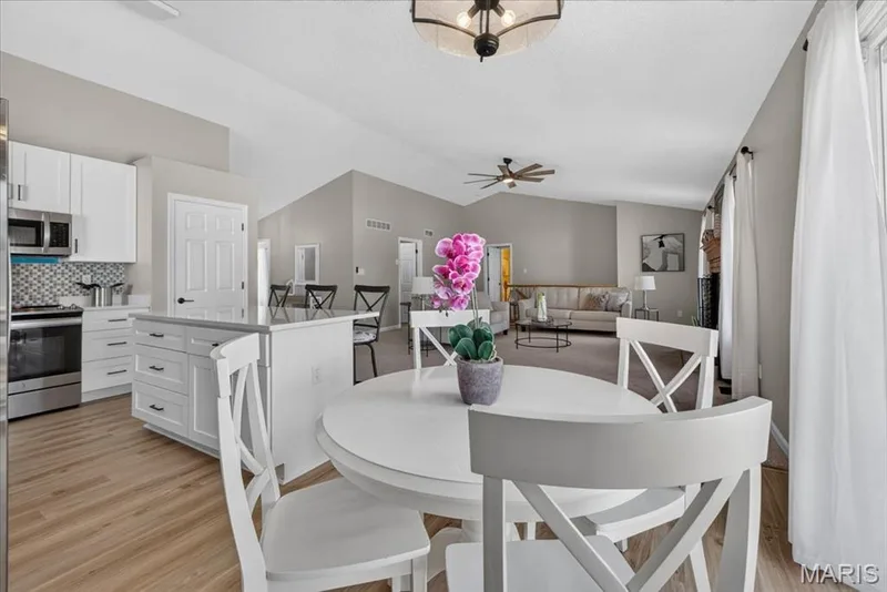 Open-concept living space featuring wood-finish flooring, vaulted ceilings, and a kitchen with white cabinetry — 89 Gregory Court, Wentzville, MO 63385