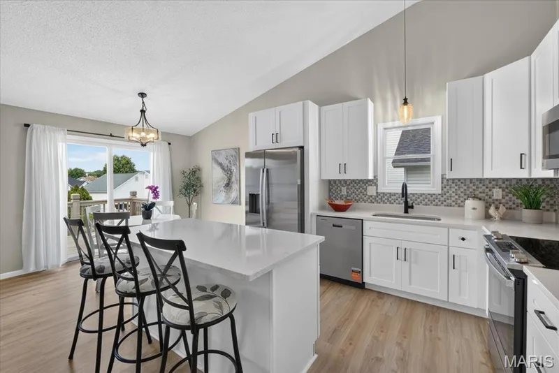 Vaulted ceiling, white shaker cabinetry, stainless steel appliances, patterned tile backsplash, and a kitchen island with a white countertop — 89 Gregory Court, Wentzville, MO 63385