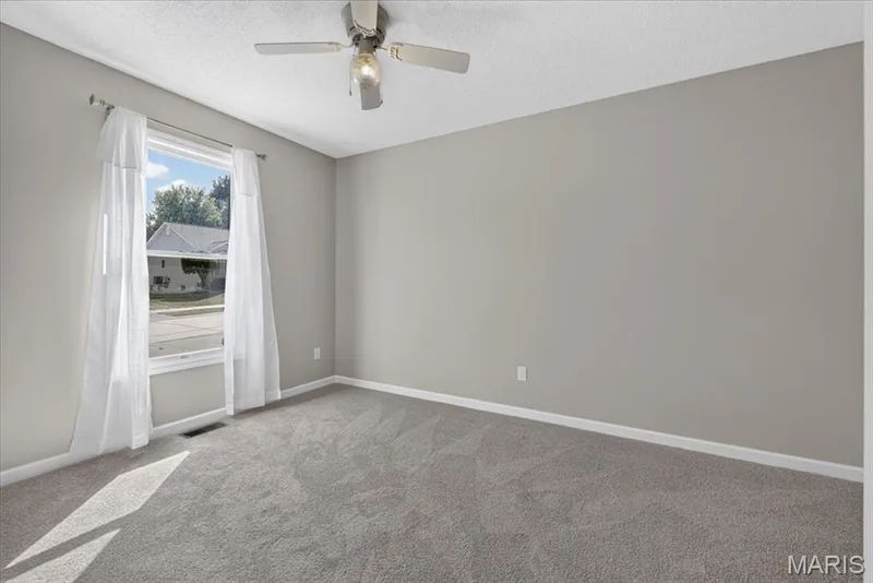 Light gray wall paint, textured ceiling, ceiling fan with integrated lighting, window with white trim, and gray carpeting — 89 Gregory Court, Wentzville, MO 63385