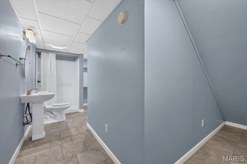 Pedestal sink, wall-mounted light fixture, tiled flooring, drop ceiling, and walk-in shower — 89 Gregory Court, Wentzville, MO 63385