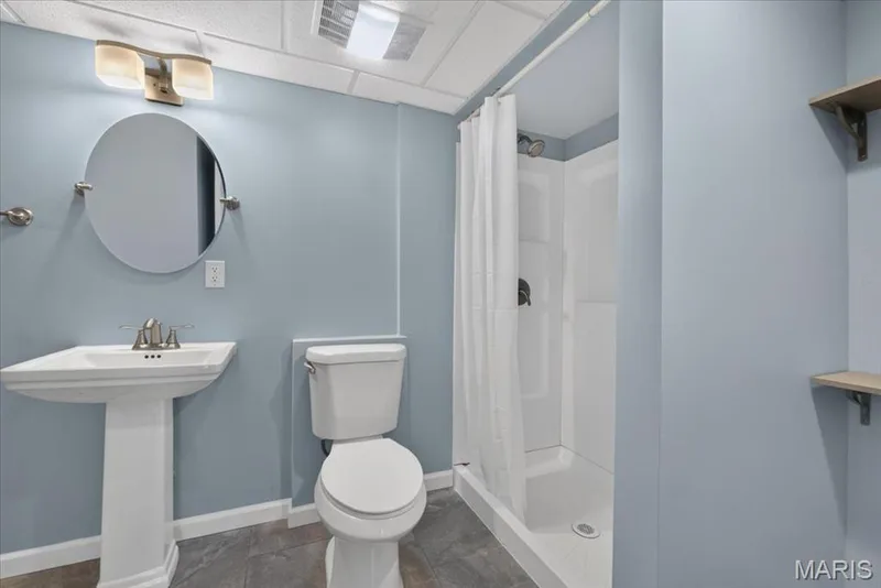 Pedestal sink with brushed nickel faucet, oval mirror, shower stall with white surround, and built-in shelving — 89 Gregory Court, Wentzville, MO 63385