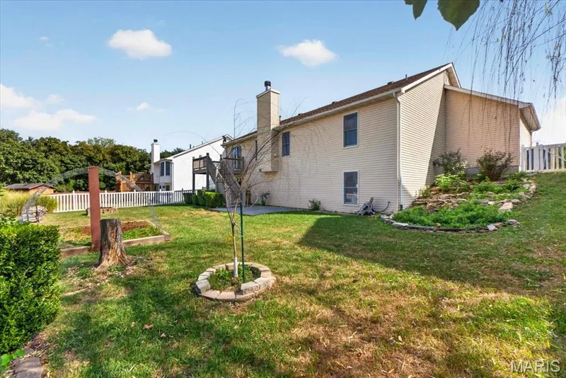 Expansive rear yard featuring green lawn, white picket fencing, and a tiered garden bed with stone edging — 89 Gregory Court, Wentzville, MO 63385