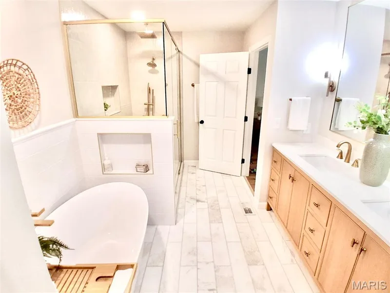 Freestanding soaking tub, walk-in shower with glass enclosure, dual vanity with wood-finish cabinetry, white countertop, and tiled flooring — 1674 Old Baxter Road, Chesterfield, MO 63017