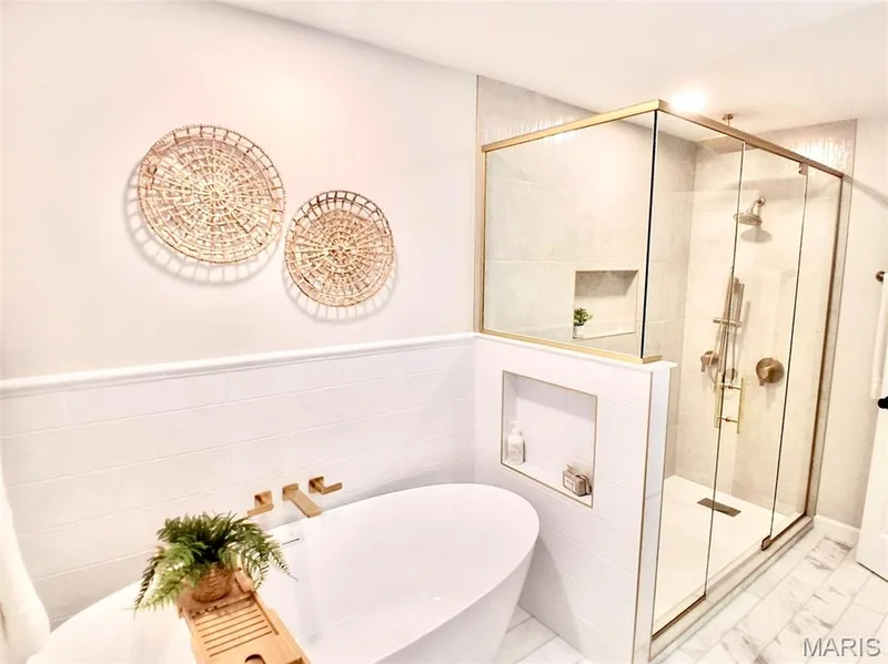 Freestanding soaking tub with a wall-mounted faucet, glass-enclosed shower with gold-finish fixtures, and marble-look tile flooring — 1674 Old Baxter Road, Chesterfield, MO 63017