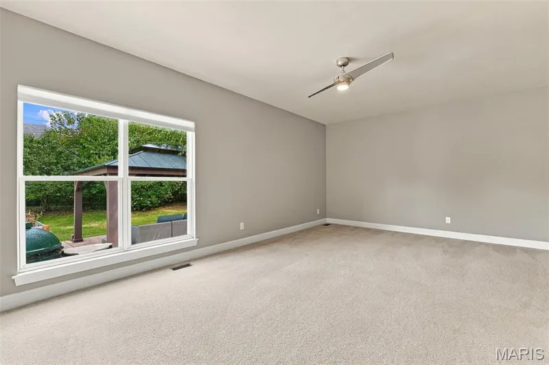 Spacious main floor In-Law Suite with ceiling fan with integrated lighting, neutral wall paint, light-colored carpeting, large window with outdoor gazebo visible — 1000 Gardenbridge Place, St Charles, MO 63303