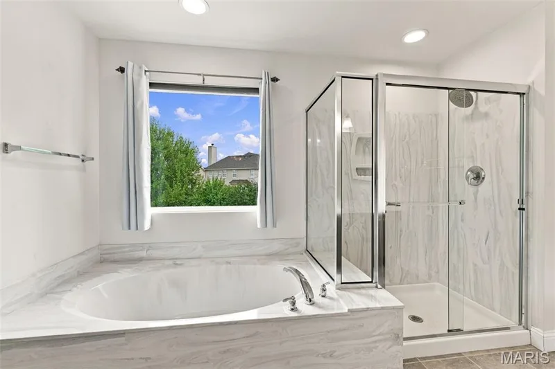 Soaking tub with a polished chrome faucet, large glass-enclosed shower with a rainfall showerhead, recessed lighting, and a window providing natural illumination — 1000 Gardenbridge Place, St Charles, MO 63303