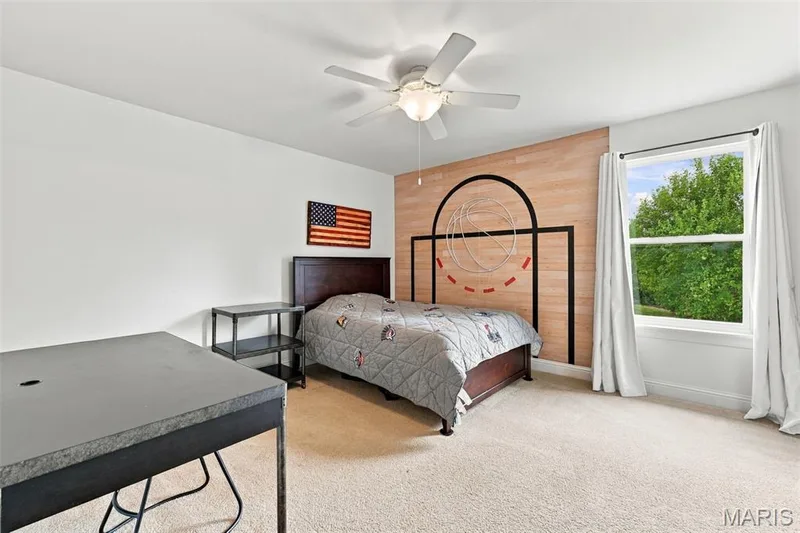 Carpeted room with a large window, a ceiling fan with integrated lighting, and a wood-paneled accent wall — 1000 Gardenbridge Place, St Charles, MO 63303