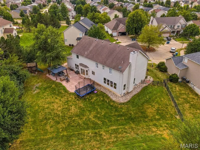 Expansive backyard featuring a paver patio with a built-in pergola, abundant fruit trees, and a two-story residential structure with bay window — 1000 Gardenbridge Place, St Charles, MO 63303