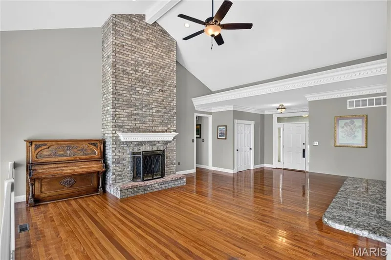 Vaulted ceiling with a ceiling fan, a full-height brick fireplace, wood-finish flooring, and crown molding — 17711 Birch Leaf Court, Chesterfield, MO 63005
