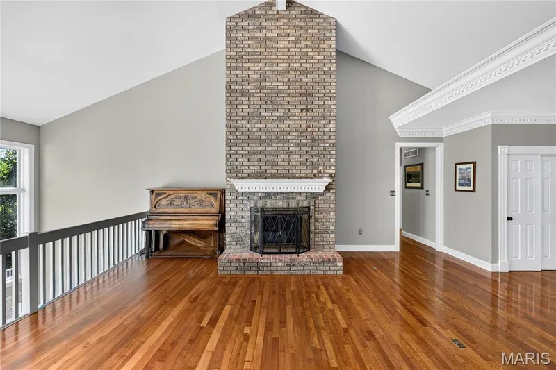 Vaulted ceiling with decorative crown molding, brick fireplace with mantel, polished wood flooring, and white paneled doors — 17711 Birch Leaf Court, Chesterfield, MO 63005