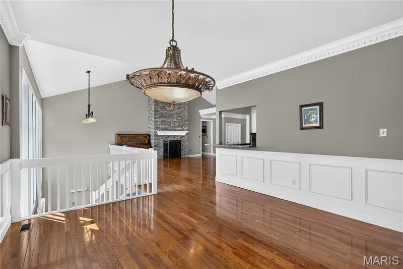 Vaulted ceiling with an ornate chandelier, hardwood flooring, detailed crown molding, a stone-surround fireplace, and wainscoting — 17711 Birch Leaf Court, Chesterfield, MO 63005