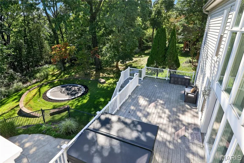 Expansive wood-finish deck with white railings, featuring a spa and direct access to a landscaped backyard with a manicured lawn and mature trees — 17711 Birch Leaf Court, Chesterfield, MO 63005
