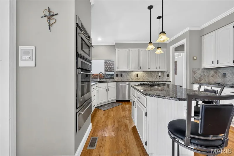 Kitchen featuring wood-finish flooring, white cabinetry, a center island with dark countertops, stainless steel appliances, and pendant lighting — 17711 Birch Leaf Court, Chesterfield, MO 63005