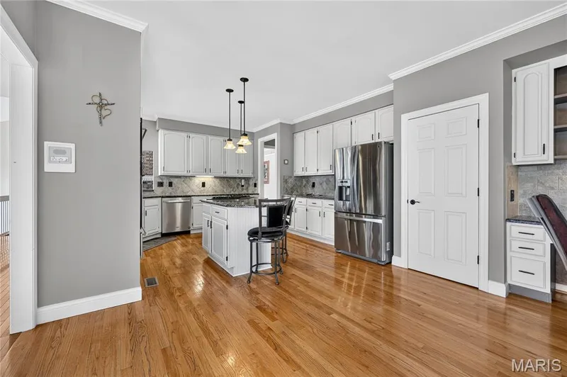Kitchen featuring hardwood flooring, white cabinetry, a center island with pendant lighting, stainless steel appliances, and a tiled backsplash — 17711 Birch Leaf Court, Chesterfield, MO 63005