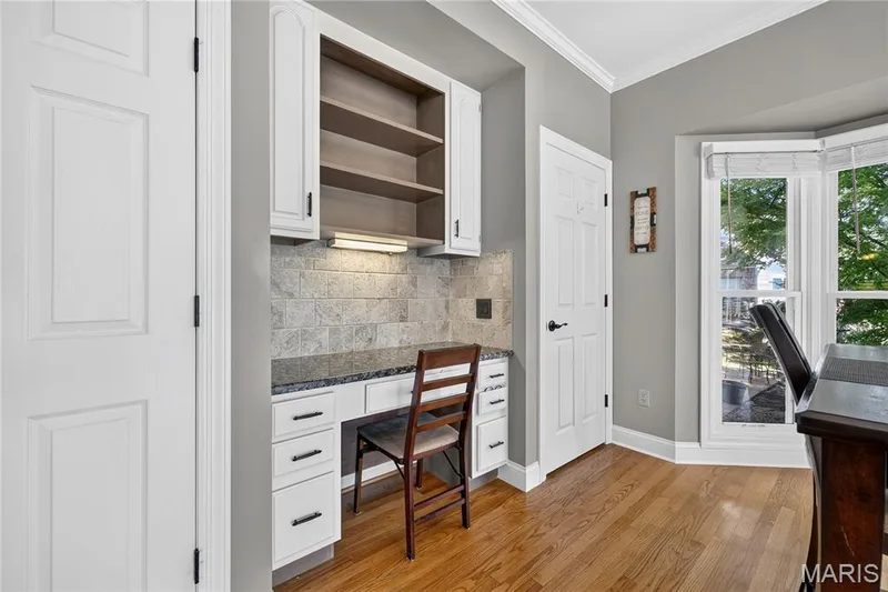Built-in desk area featuring white cabinetry, a stone-tile backsplash, and solid surface countertop — 17711 Birch Leaf Court, Chesterfield, MO 63005