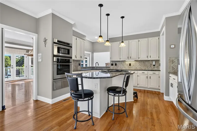 Kitchen featuring wood-finish flooring, white cabinetry, stainless steel double ovens, a center island with bar seating, and a tiled backsplash — 17711 Birch Leaf Court, Chesterfield, MO 63005