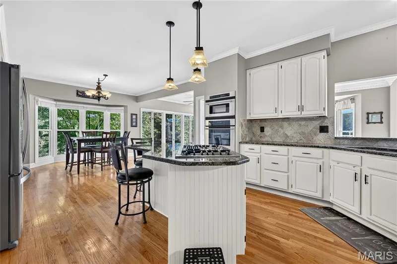 White cabinetry with dark hardware, built-in double ovens, dark countertops, a tiled backsplash, and wood-finish flooring — 17711 Birch Leaf Court, Chesterfield, MO 63005