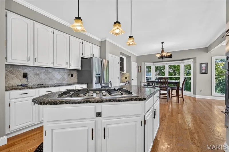 Kitchen featuring white cabinetry, granite countertops, tile backsplash, built-in stainless steel appliances, and hardwood flooring — 17711 Birch Leaf Court, Chesterfield, MO 63005