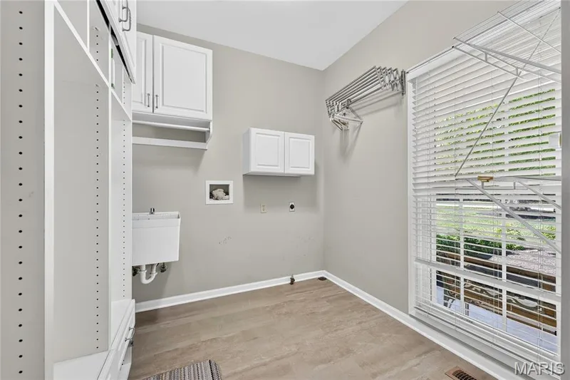 Laundry room featuring wood-finish flooring, white cabinetry, a utility sink, and a large window — 17711 Birch Leaf Court, Chesterfield, MO 63005