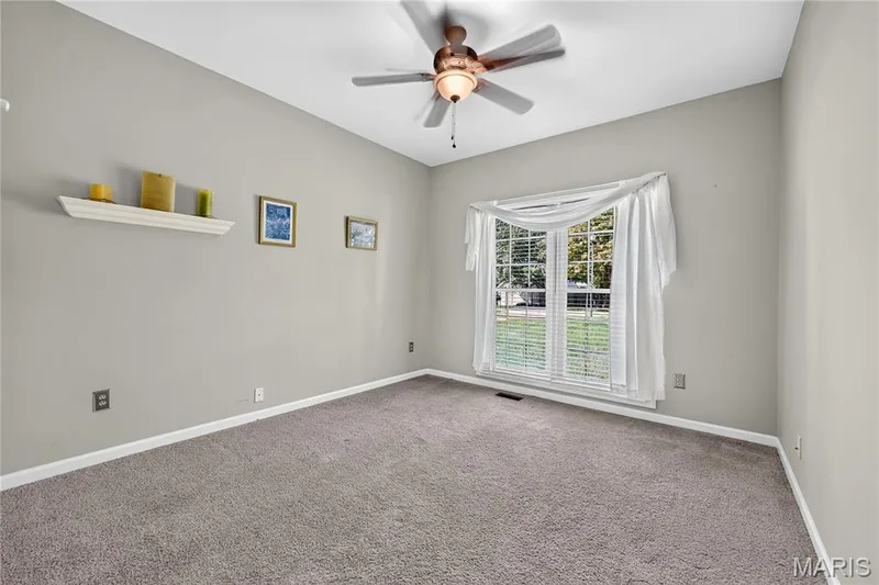 Carpeted room featuring a ceiling fan with integrated lighting, a large window with blinds, and neutral wall tones — 17711 Birch Leaf Court, Chesterfield, MO 63005