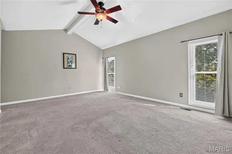 Vaulted ceiling with an exposed beam, ceiling fan with light fixture, gray carpeting, and two windows with blinds — 17711 Birch Leaf Court, Chesterfield, MO 63005