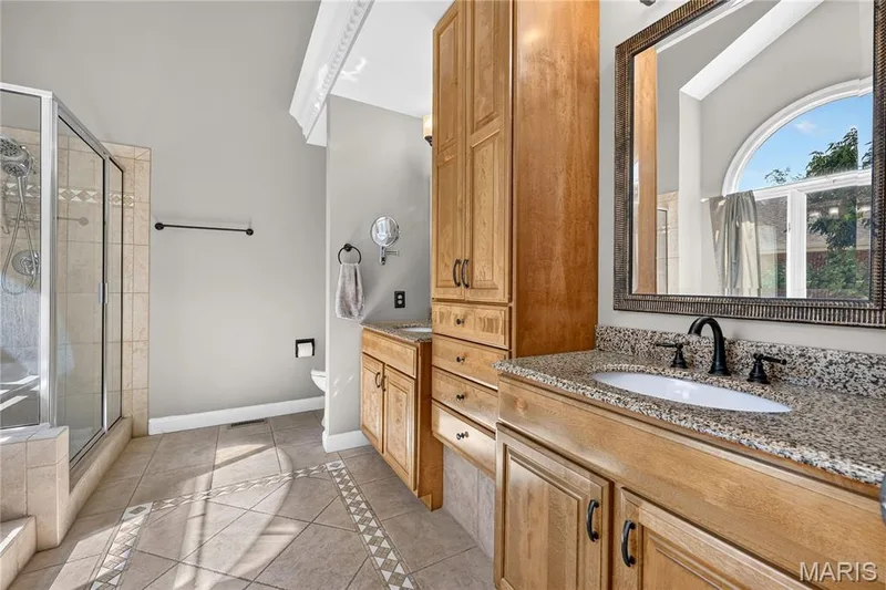 Wood-finish cabinetry with a built-in linen tower, granite-style countertop, and tile flooring with decorative inlay — 17711 Birch Leaf Court, Chesterfield, MO 63005
