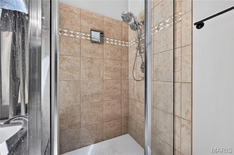 Tiled shower enclosure featuring a multi-function showerhead, glass door, and decorative tile accent band — 17711 Birch Leaf Court, Chesterfield, MO 63005
