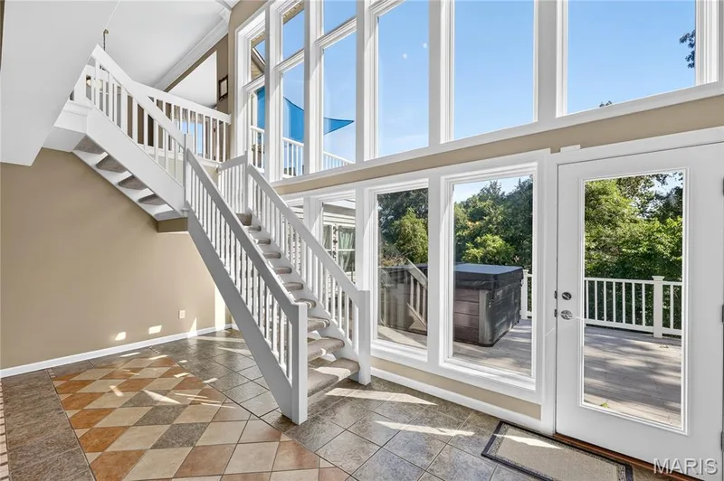 Two-story wall of windows, white painted staircase with carpeted treads, patterned tile flooring, and a private deck with a hot tub — 17711 Birch Leaf Court, Chesterfield, MO 63005