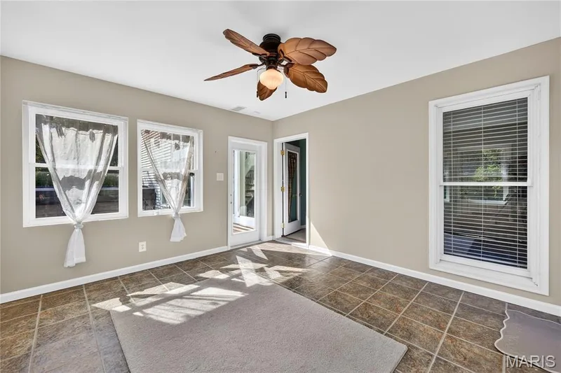 Neutral wall finishes, multiple windows, ceiling fan with light fixture, tiled flooring, and a glass-paneled door — 17711 Birch Leaf Court, Chesterfield, MO 63005