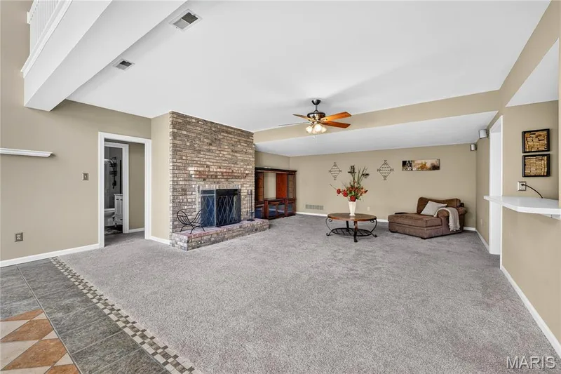 Spacious living area featuring a brick fireplace, ceiling fan, carpet flooring, and a tiled entryway — 17711 Birch Leaf Court, Chesterfield, MO 63005
