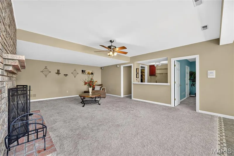 Carpeted living area featuring a brick fireplace, ceiling fan, and a pass-through window to an additional space — 17711 Birch Leaf Court, Chesterfield, MO 63005