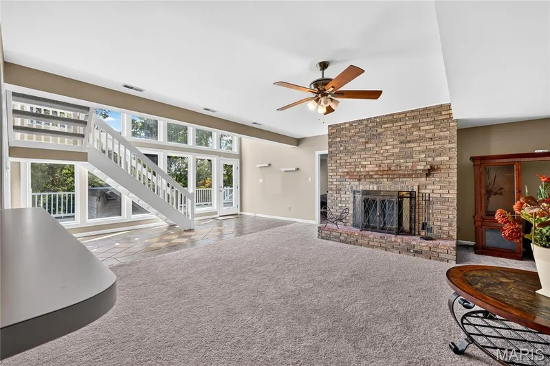 Expansive living area featuring a brick fireplace, ceiling fan, and large windows — 17711 Birch Leaf Court, Chesterfield, MO 63005
