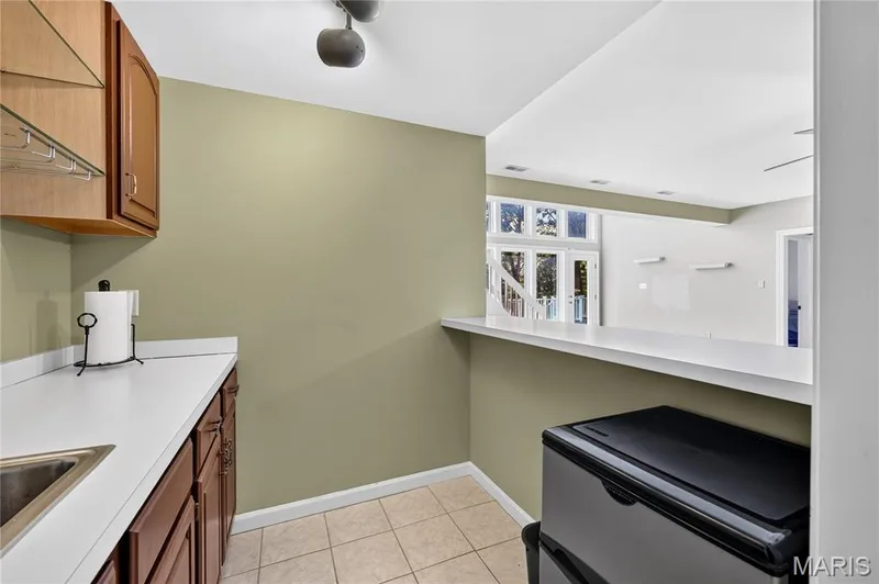 Kitchenette featuring wood-finish cabinetry, a stainless steel sink, and light-toned countertops — 17711 Birch Leaf Court, Chesterfield, MO 63005